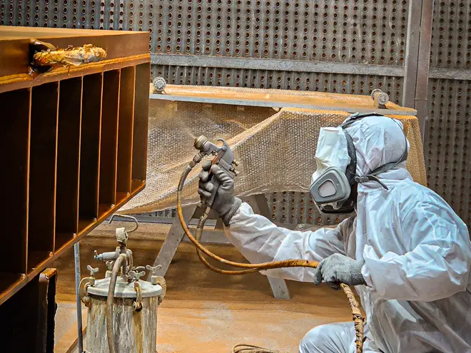 Industrial painter in protective suit spray-coating a steel structure